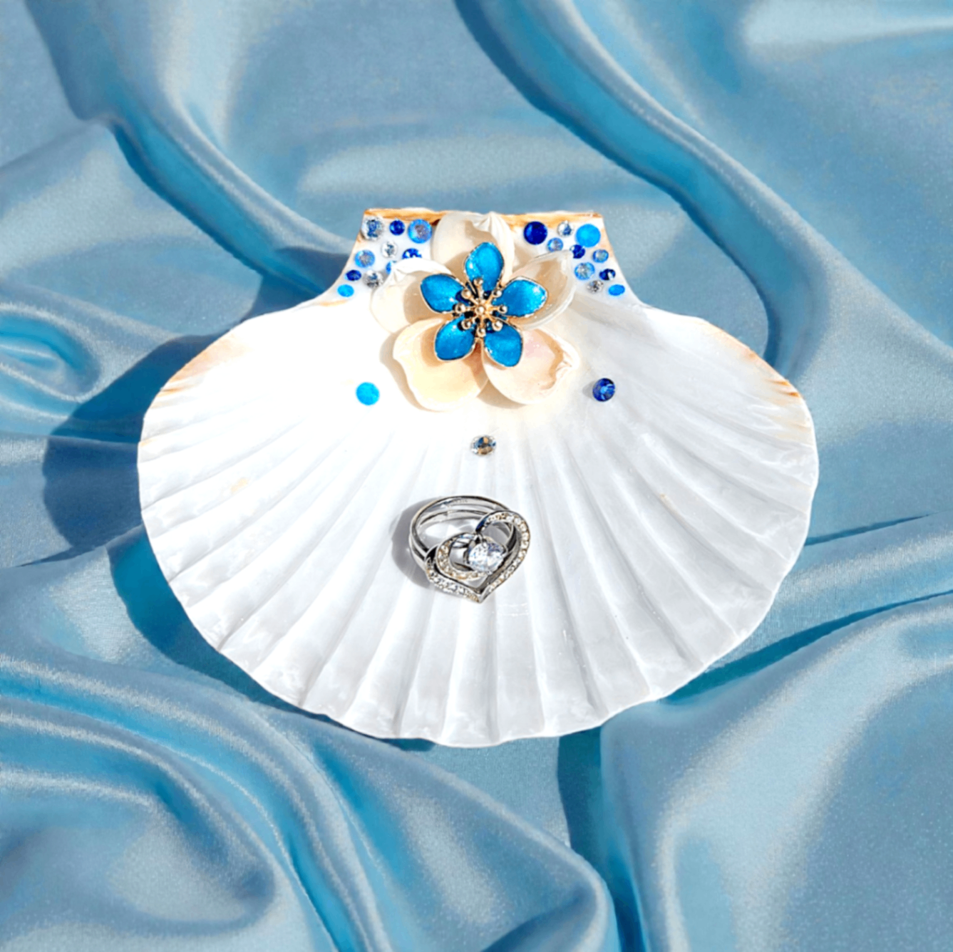 White shell ring dish on blue satin with a vivid blue floral accent.