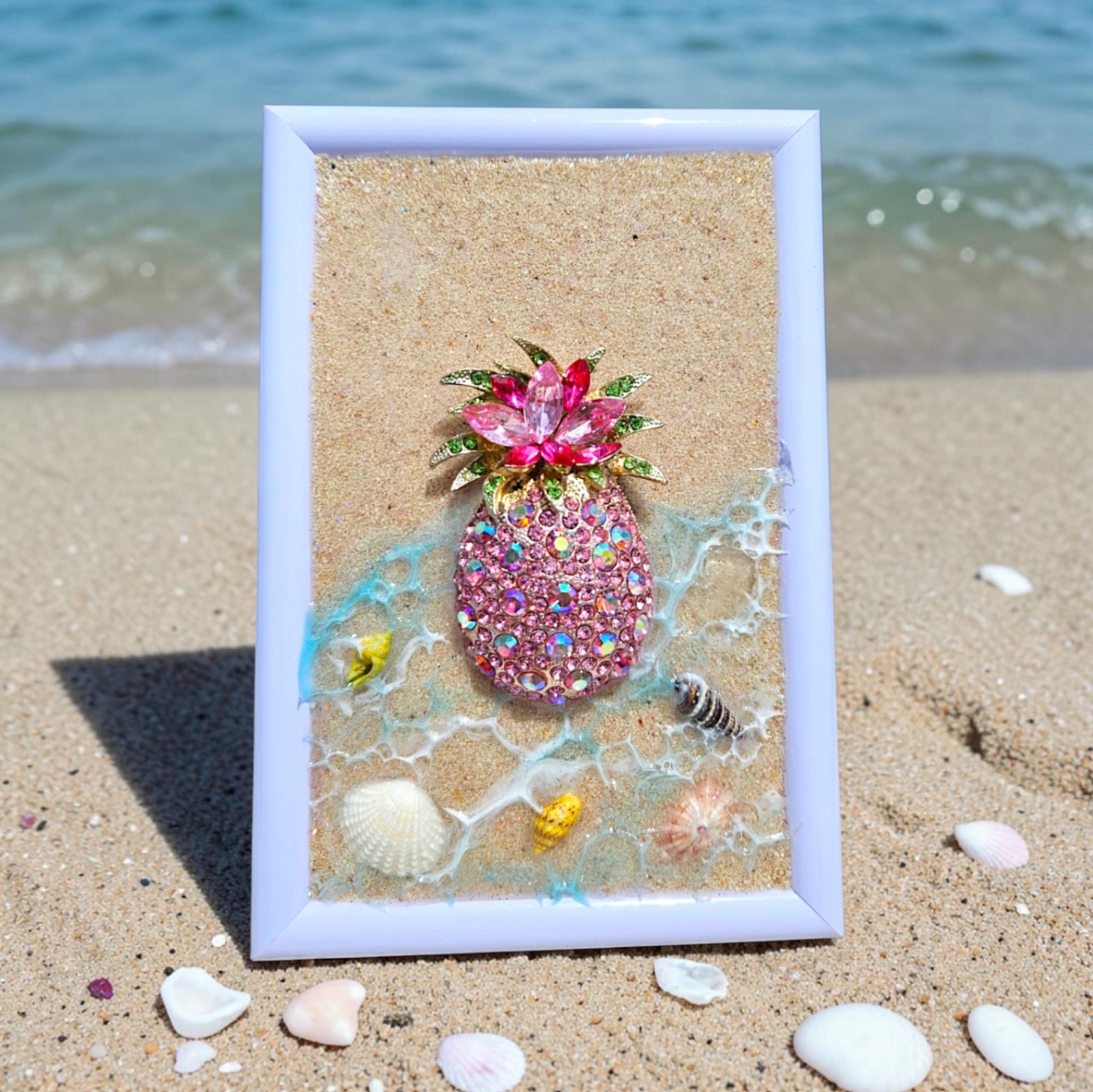 White frame with sand, resin waves, and a sparkling pink jeweled pineapple.