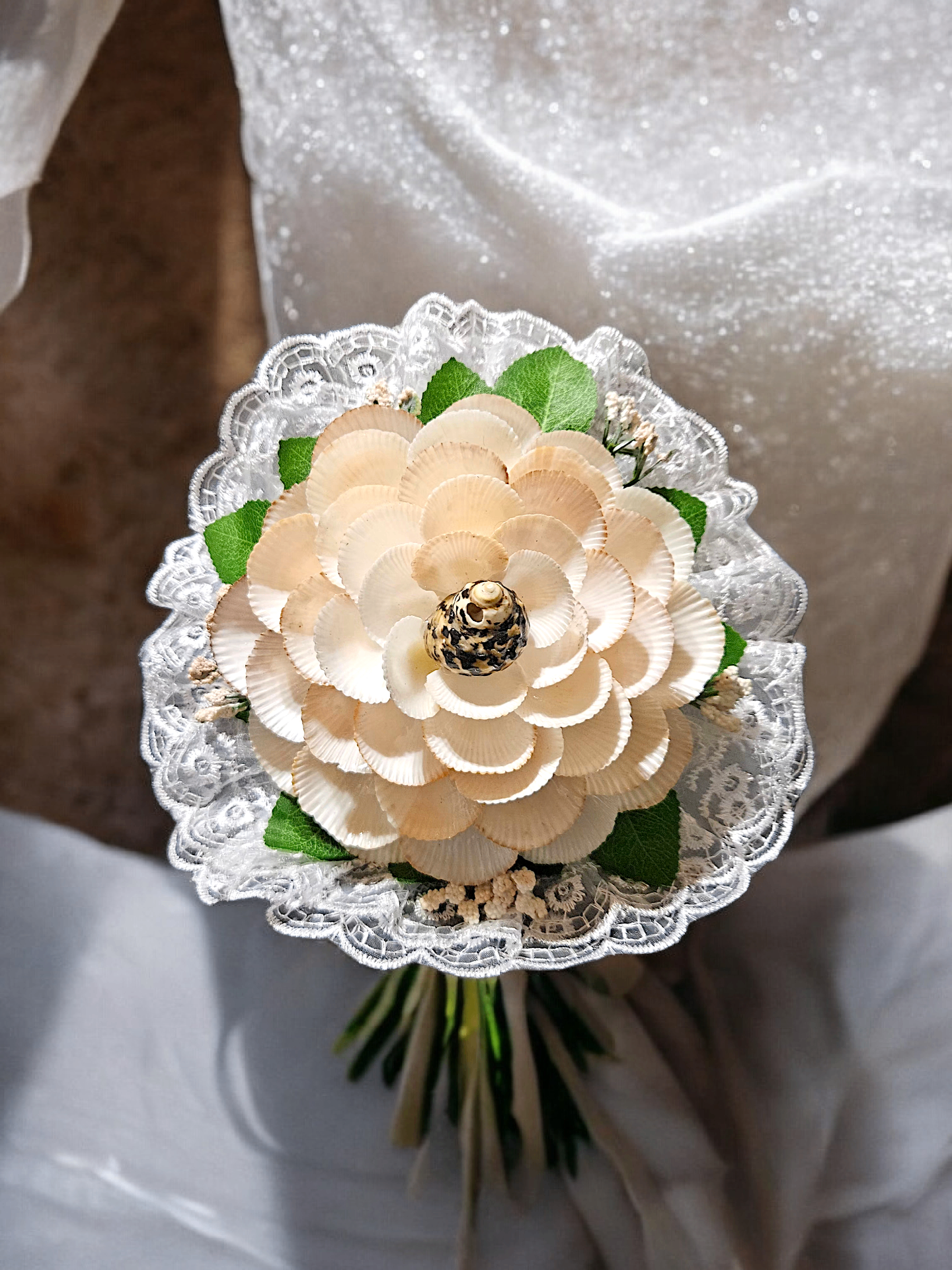 Neutral shell flower bouquet wrapped with lace and greenery.