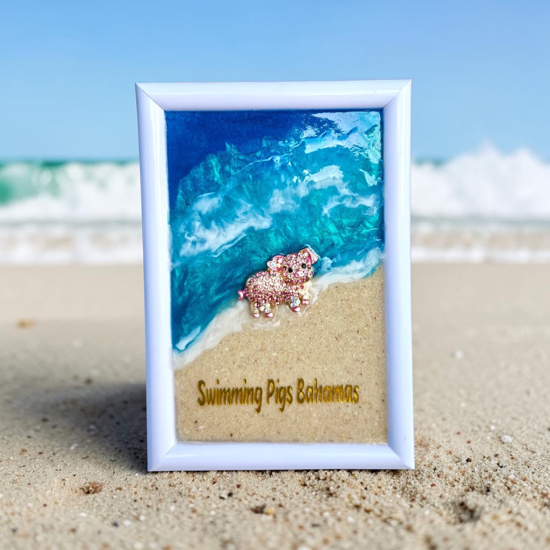 White frame with turquoise resin waves and a pink jeweled pig with 'Swimming Pigs Bahamas' lettering.