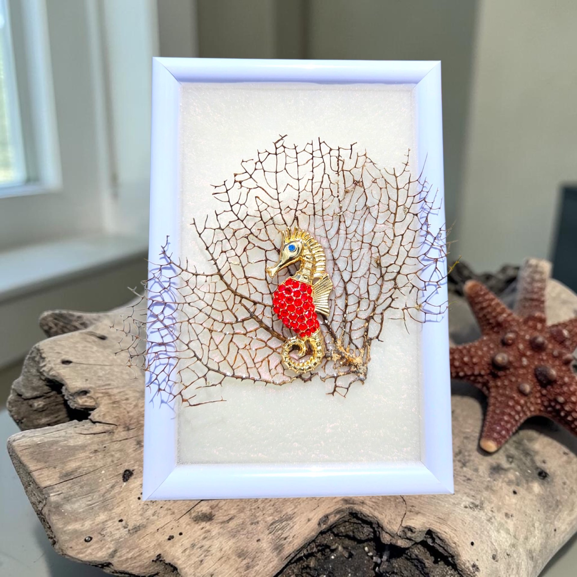 White frame featuring a gold and red jeweled seahorse on a natural sea fan coral backdrop.