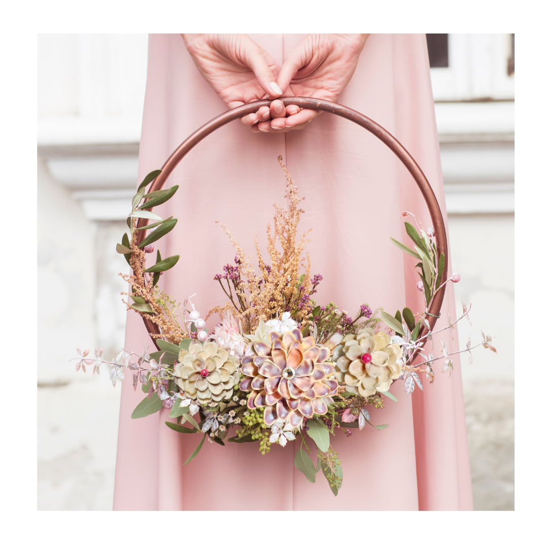 Floral ring arrangement with shell flowers in blush and lavender tones.